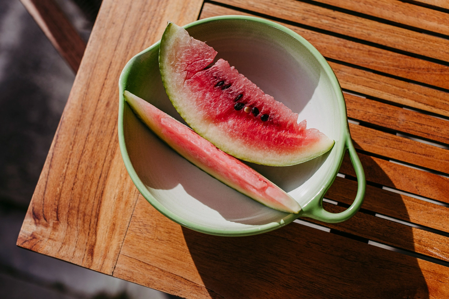 Keramik Atelier Melis - Töpferkurse - Zwei Wassermelonenscheiben in einer grünen Schüssel auf einem Holztisch.
