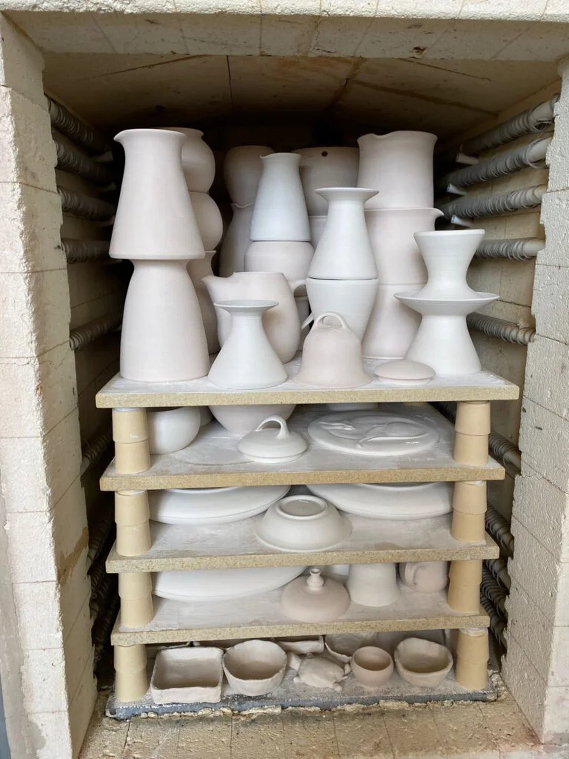Keramik Atelier Melis - Töpferkurse - Ein Brennofen, gefüllt mit verschiedenen weißen, unglasierten Keramikstücken, die auf Holzregalen gestapelt sind und zum Brennen bereitliegen.