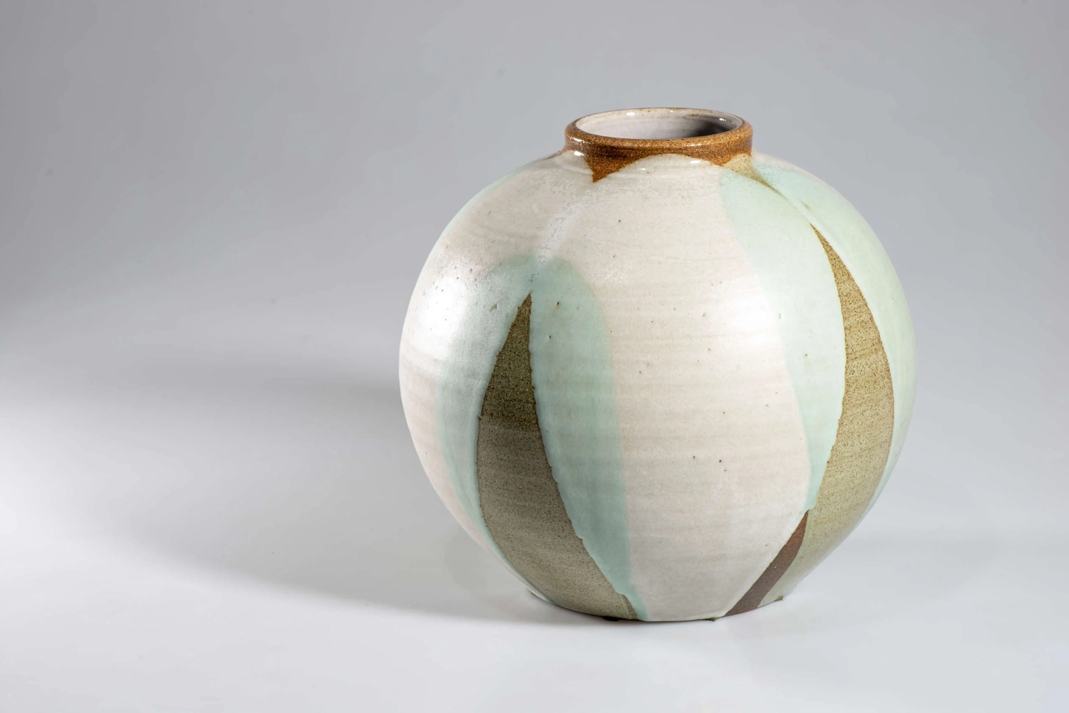 Keramik Atelier Melis - Töpferkurse - Eine runde, gedrungene Keramikvase mit schmaler Öffnung, verziert mit vertikalen Segmenten aus weißer, hellgrüner und olivbrauner Glasur.