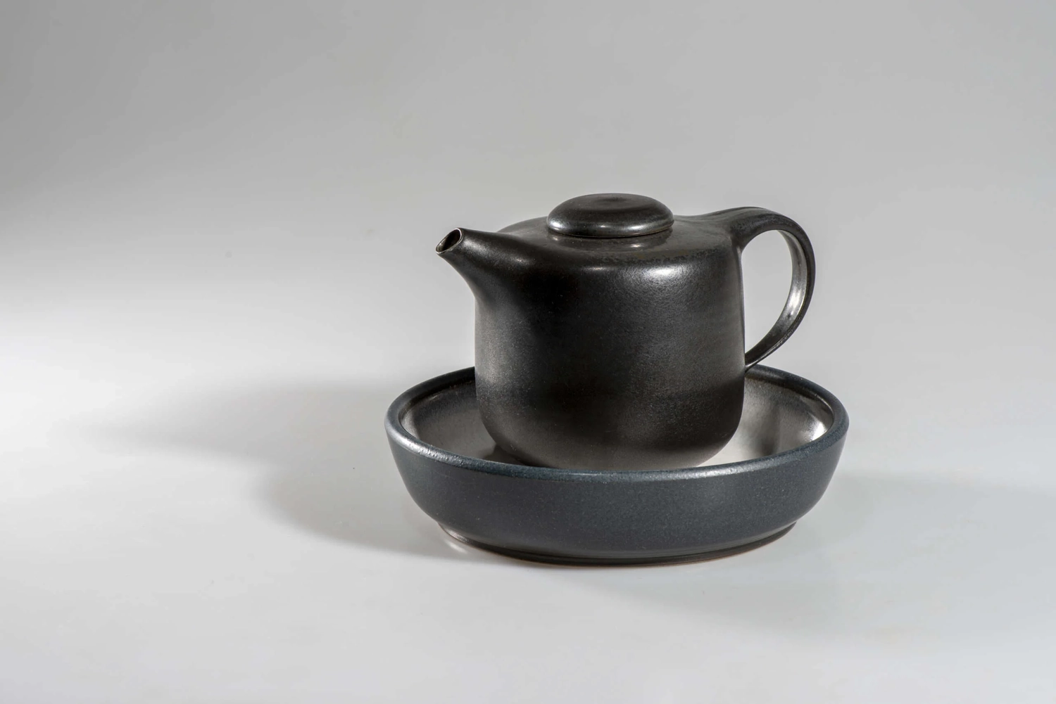 Keramik Atelier Melis - Töpferkurse - Eine schwarze Teekanne in einer schwarzen Schale oder Untertasse.