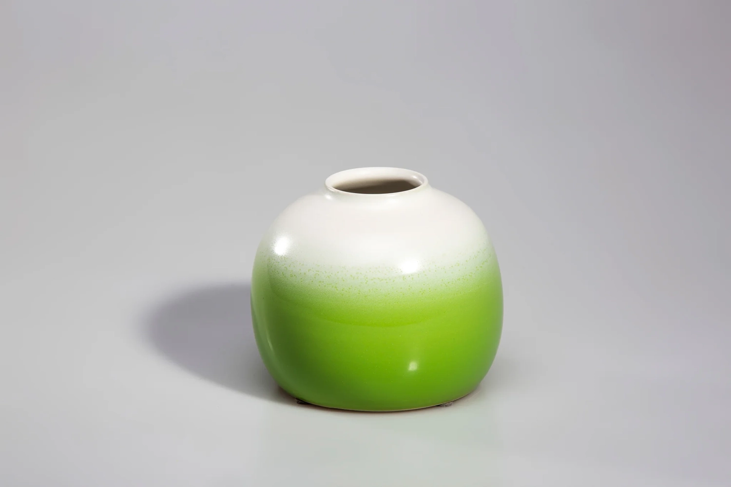 Keramik Atelier Melis - Töpferkurse - Eine kleine, kugelförmige Keramikvase mit weißem oberen Rand, der in einen hellgrünen unteren Rand übergeht.