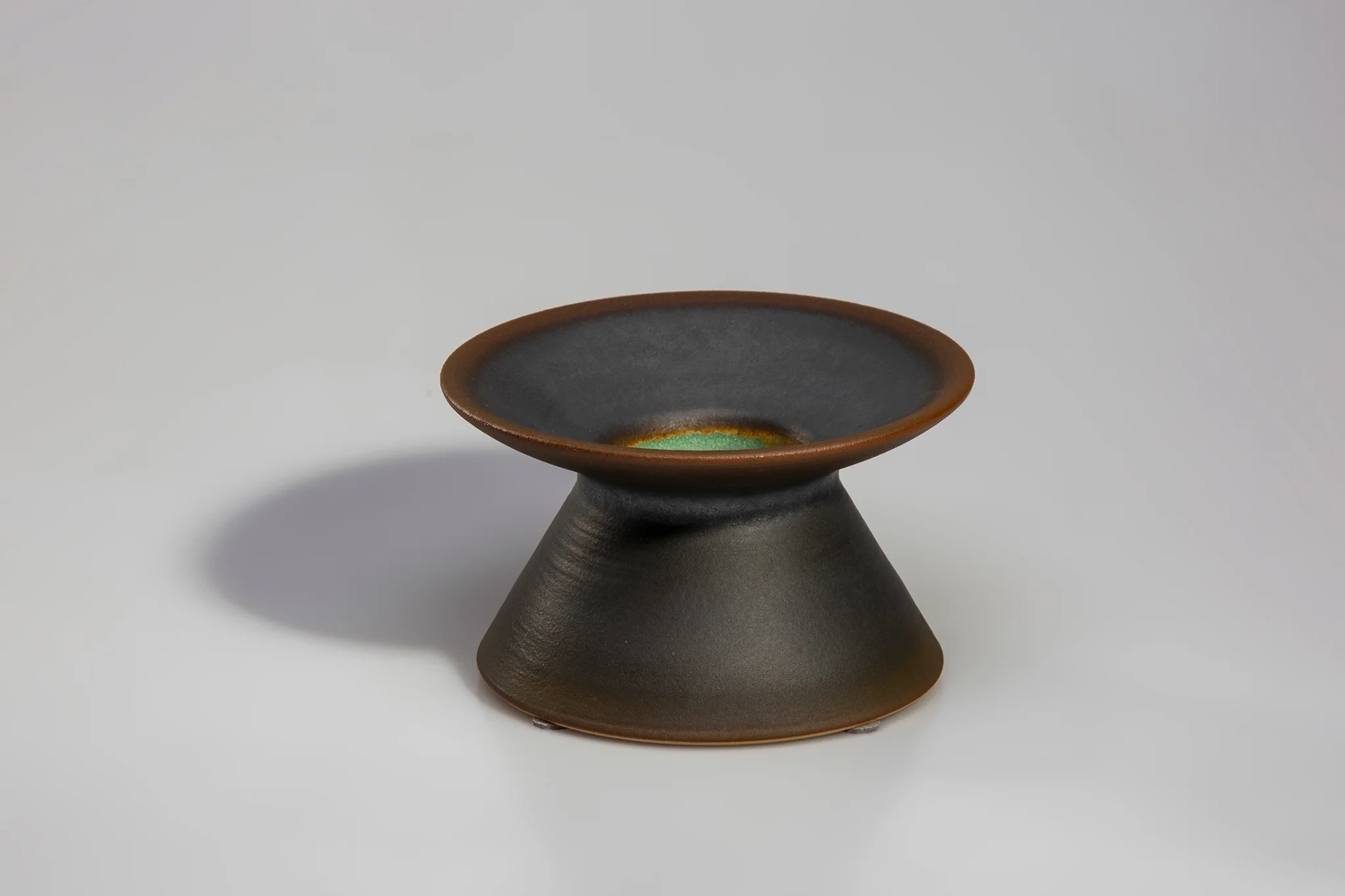 Keramik Atelier Melis - Töpferkurse - Ein kleiner, dunkelbrauner oder schwarz glasierter Keramikkerzenhalter mit breiter, flacher Oberseite und konischem Sockel.