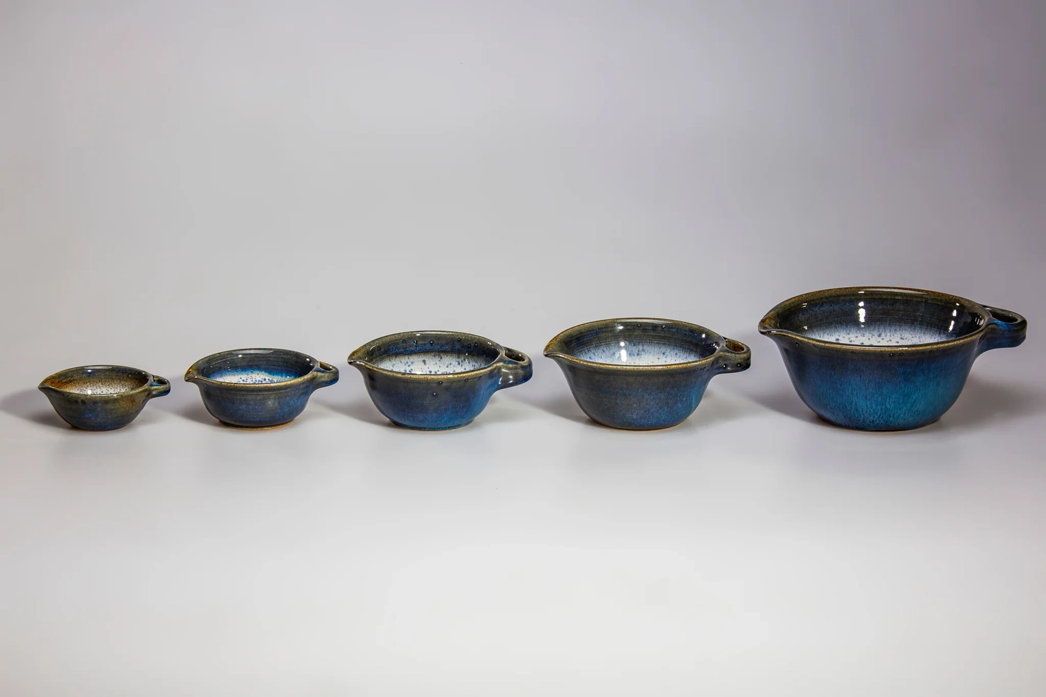 Keramik Atelier Melis - Töpferkurse - Set aus fünf handgefertigten, blau-weißen Keramikschalen in zunehmender Größe, die in einer Reihe aufgestellt sind.