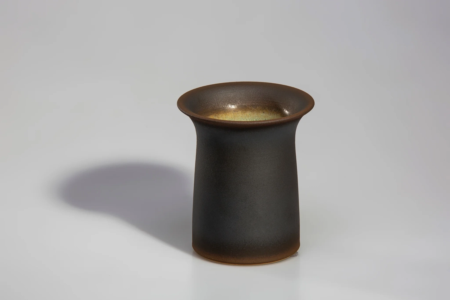 Keramik Atelier Melis - Töpferkurse - Eine dunkelbraune, trompetenförmige Keramikvase mit ausladendem Rand und Boden sowie einer helleren, gelblich-goldenen Innenglasur.