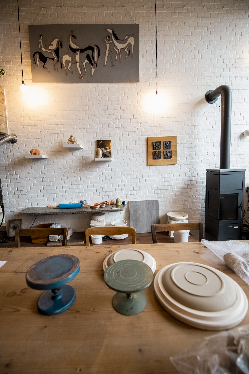 Keramik Atelier Melis - Töpferkurse - Das Interieur eines Töpferateliers mit einem Holztisch voller Keramikteller, einer Werkbank und einem schwarzen Holzofen.