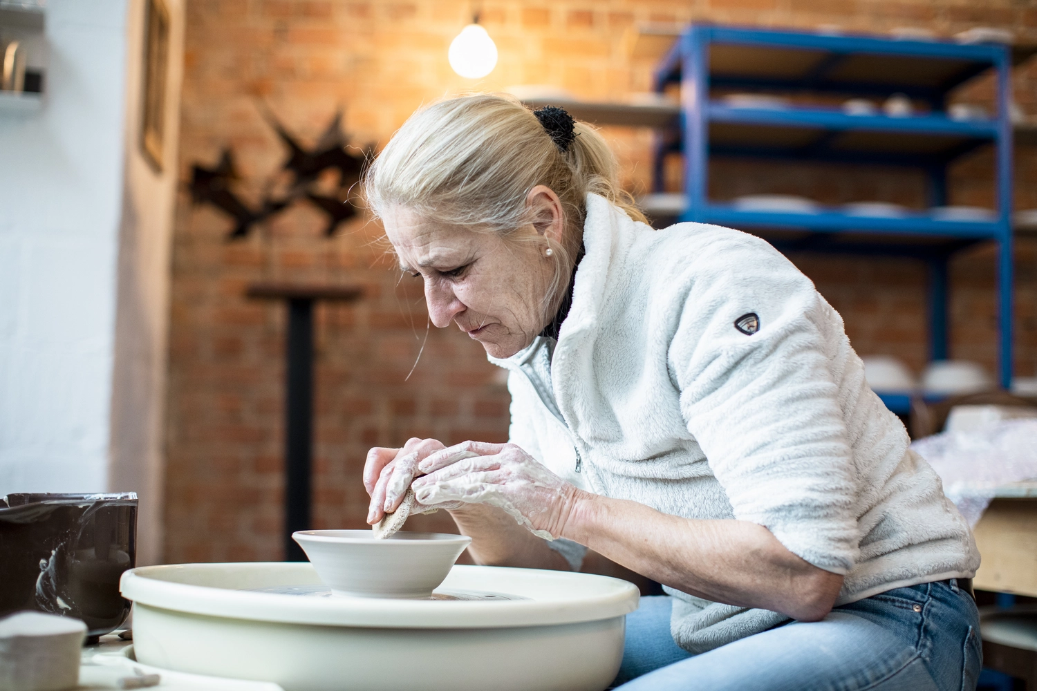 Keramik Atelier Melis - Töpferkurse - Eine Frau formt einen Tontopf auf einer Töpferscheibe.