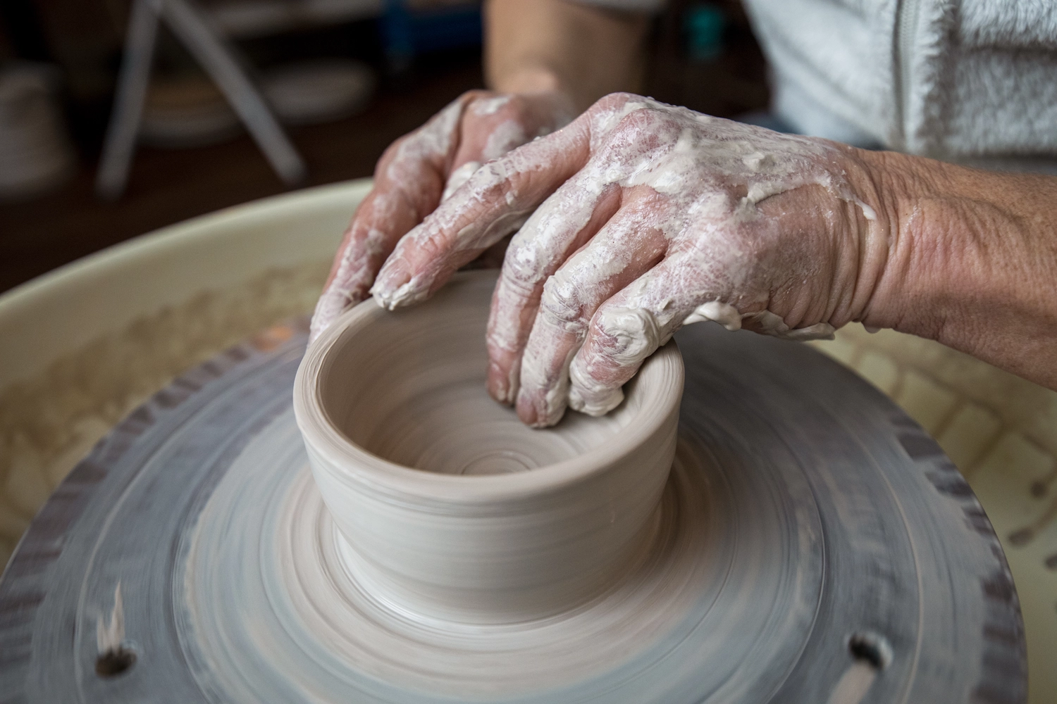 Keramik Atelier Melis - Töpferkurse - Die Hände einer Person formen Ton auf einer Töpferscheibe, ein Vorgang, der als „Töpfern“ bekannt ist.