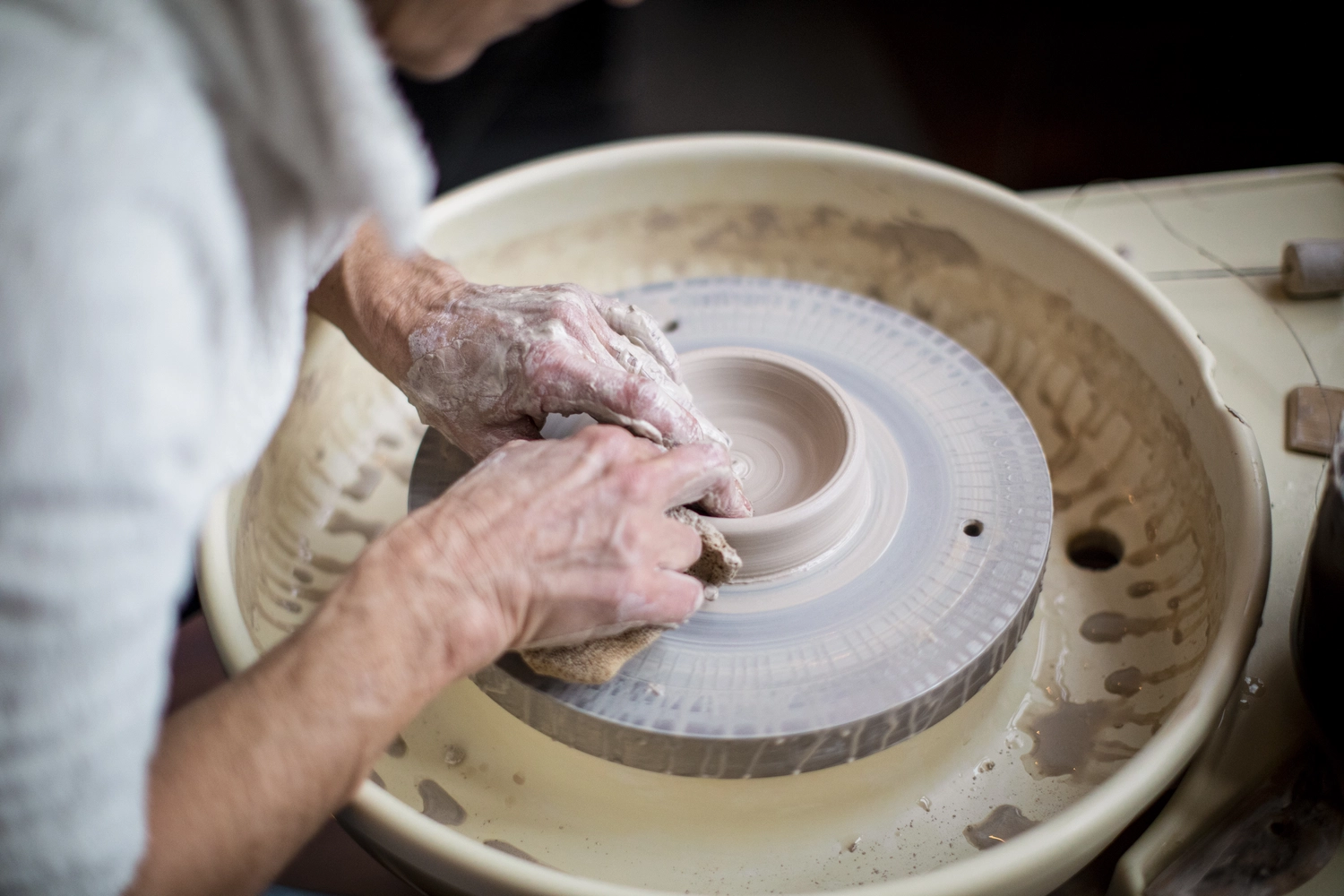 Keramik Atelier Melis - Töpferkurse - Die Hände einer Person formen Ton auf einer Töpferscheibe, ein Vorgang, der als „Töpfern“ bekannt ist.