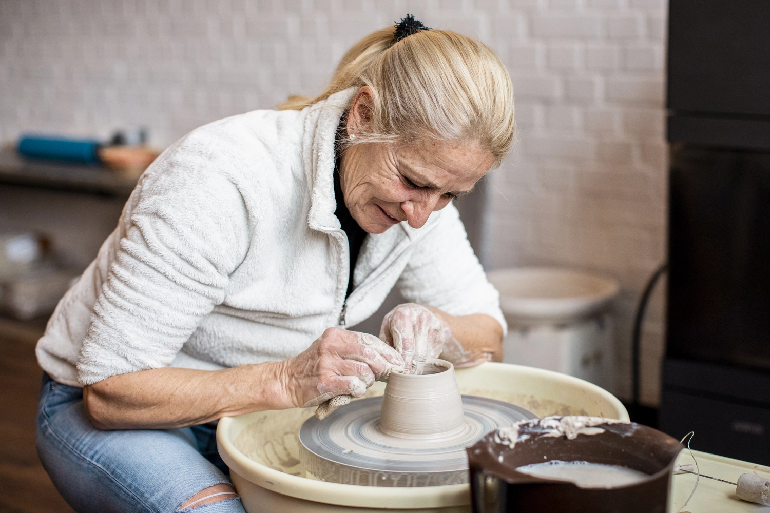 Keramik Atelier Melis - Töpferkurse - Eine Frau formt einen Tontopf auf einer Töpferscheibe.