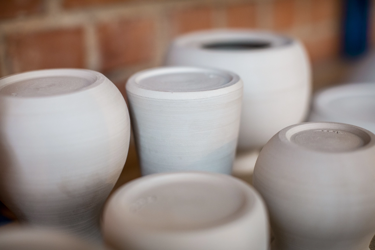 Keramik Atelier Melis - Töpferkurse - Eine Nahaufnahme mehrerer weißer, ungebrannter Keramiktöpfe und -gefäße in verschiedenen runden Formen und Größen.