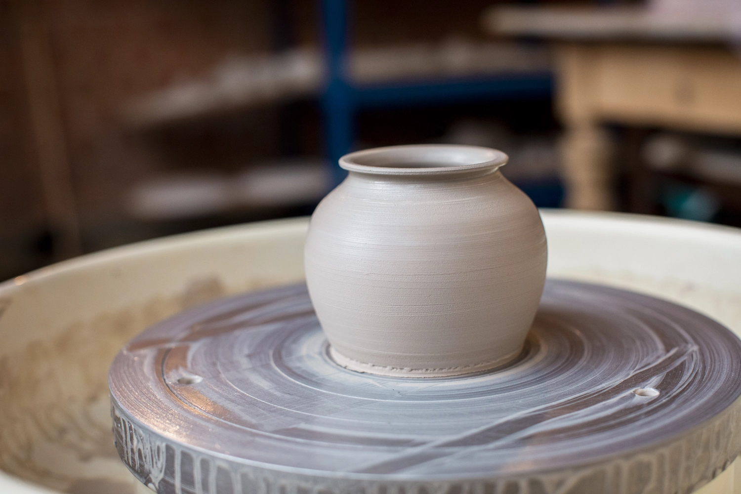 Keramik Atelier Melis - Töpferkurse - Ein kleiner, hellfarbiger Keramiktopf wird auf einer Töpferscheibe geformt.